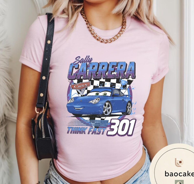 Puede incluir: Camiseta rosa claro con un dise&ntilde;o de Sally Carrera de la pel&iacute;cula Cars. El dise&ntilde;o incluye el texto "Sally Carrera", "Cars" y "Think Fast 301" con una ilustraci&oacute;n de un coche azul.