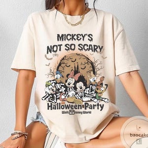 May include: Beige t-shirt featuring a Halloween-themed graphic. The design includes Mickey Mouse, Minnie Mouse, Donald Duck, and Goofy in skeleton costumes, with the text "Mickey's Not So Scary Halloween Party" and "Walt Disney World".