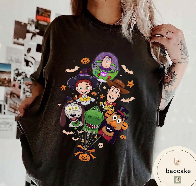 Pode incluir: Uma t-shirt preta de manga curta com uma impress&atilde;o gr&aacute;fica de personagens de Toy Story vestidos com fantasias de Halloween, incluindo Buzz Lightyear, Woody, Jessie, Rex, Slinky Dog e Mr. Potato Head, todos ligados por fios a uma ab&oacute;bora.