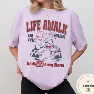 May include: A light purple t-shirt with the text "LIFE AWALK IN THE PARK" in red and white. The shirt features a cartoon image of Stitch from Disney's Lilo & Stitch, and the words "Walt Disney World".