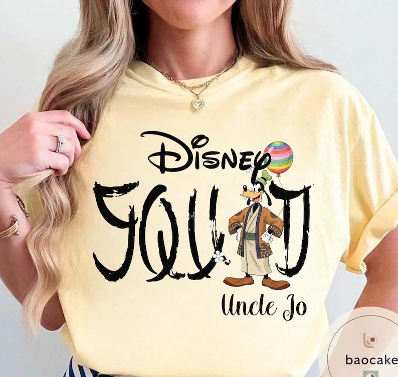 Puede incluir: Camiseta amarilla clara con la inscripci&oacute;n "Disney Goofy Uncle Jo" en escritura negra. El dise&ntilde;o incluye una imagen de dibujos animados de Goofy sosteniendo un globo de arco&iacute;ris. La camiseta tiene mangas cortas.
