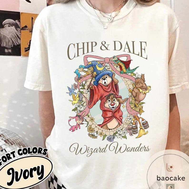 May include: Ivory-colored t-shirt featuring Chip and Dale in wizard costumes, surrounded by a floral wreath. The text "Chip & Dale" and "Wizard Wonders" are printed above and below the graphic. The shirt has a crew neck.