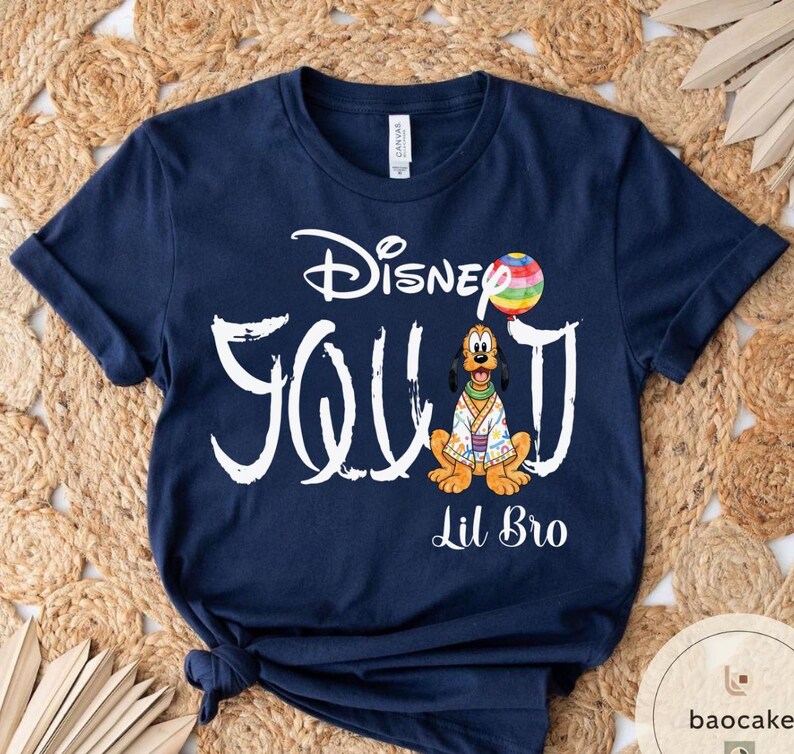 Puede incluir: Camiseta azul marino con la inscripci&oacute;n blanca "Disney Squad" y "Lil Bro". El dise&ntilde;o incluye un personaje de dibujos animados de Pluto con un atuendo colorido y un globo arco&iacute;ris.