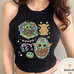 May include: A black sleeveless tank top featuring a graphic print of the character Grogu in various poses, including inside a decorative frame and holding a helmet. The design includes small stars, a green macaron, and the text GROGU in white.