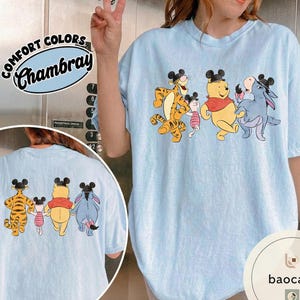 May include: Light blue Comfort Colors Chambray t-shirt featuring a graphic of Winnie the Pooh, Tigger, Piglet, and Eeyore wearing Mickey Mouse ears. The characters are walking together. The same graphic is on the back of the shirt.