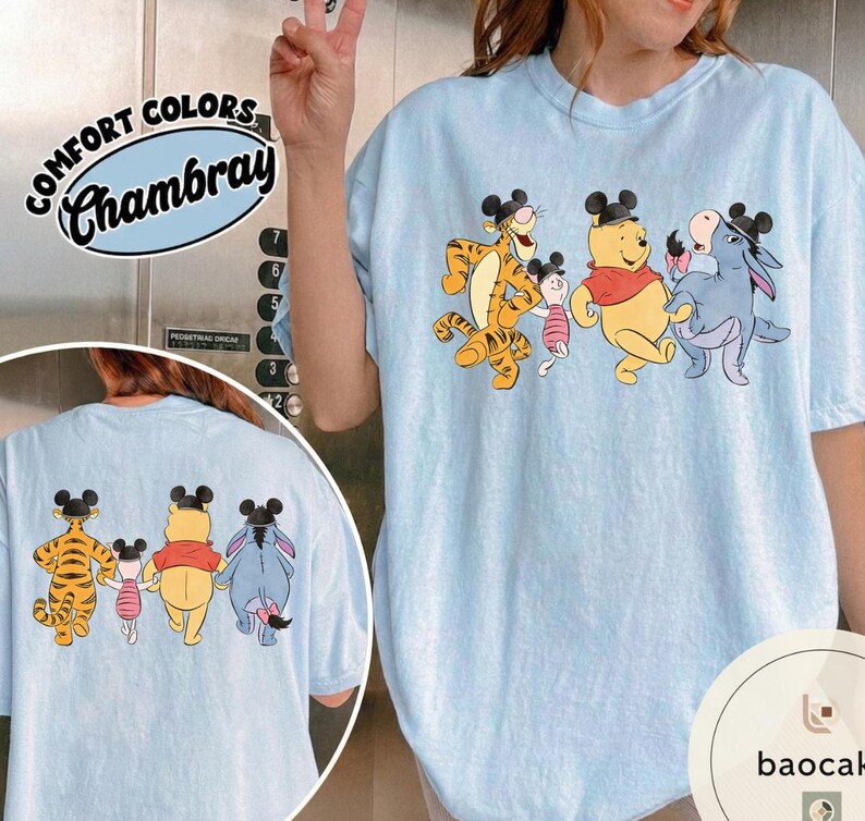 May include: Light blue Comfort Colors Chambray t-shirt featuring a graphic of Winnie the Pooh, Tigger, Piglet, and Eeyore wearing Mickey Mouse ears. The characters are walking together. The same graphic is on the back of the shirt.