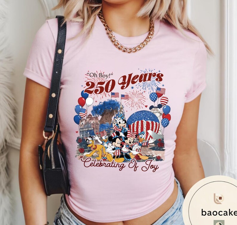 Puede incluir: Camiseta rosa claro con un dise&ntilde;o de Mickey, Minnie, Donald y Goofy celebrando. El dise&ntilde;o incluye el texto "Oh Boy! 250 Years Celebrating of Joy" con fuegos artificiales, globos y banderas americanas.