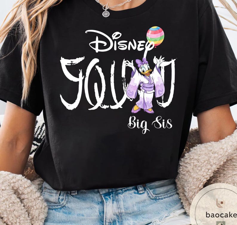 Puede incluir: Camiseta negra con el texto blanco "Disney Squad", con un dibujo de Daisy Duck con un kimono sosteniendo un globo de arco&iacute;ris. Las palabras "Big Sis" est&aacute;n debajo.