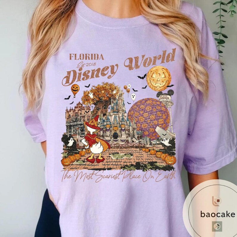 Op de afbeelding: Een lichtpaars T-shirt met een Halloween-thema Disney World-afbeelding. Het ontwerp bevat een pompoen, vleermuizen, geesten en Donald Duck in een heksenkostuum. Tekst luidt "Florida Disney World" en "The Most Scariest Place On Earth."