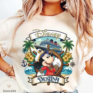 May include: Cream-colored t-shirt featuring a Disney cruise design. The graphic includes Mickey Mouse in a captain's uniform, a ship, palm trees, and the word "Destiny" on a banner. The word "Disney" is also displayed.
