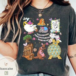 May include: Dark gray t-shirt featuring a colorful graphic with Disney characters and landmarks. The design includes images of a teapot, dogs, cats, a kangaroo, and the text "Happiest Mom on Earth."