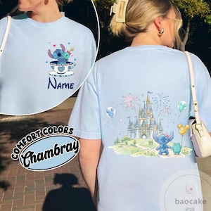 May include: Light blue t-shirt featuring Stitch in a teacup on the front and a castle scene on the back. The front has the word "Name" and the back has fireworks and balloons. The shirt is labeled "Comfort Colors Chambray".