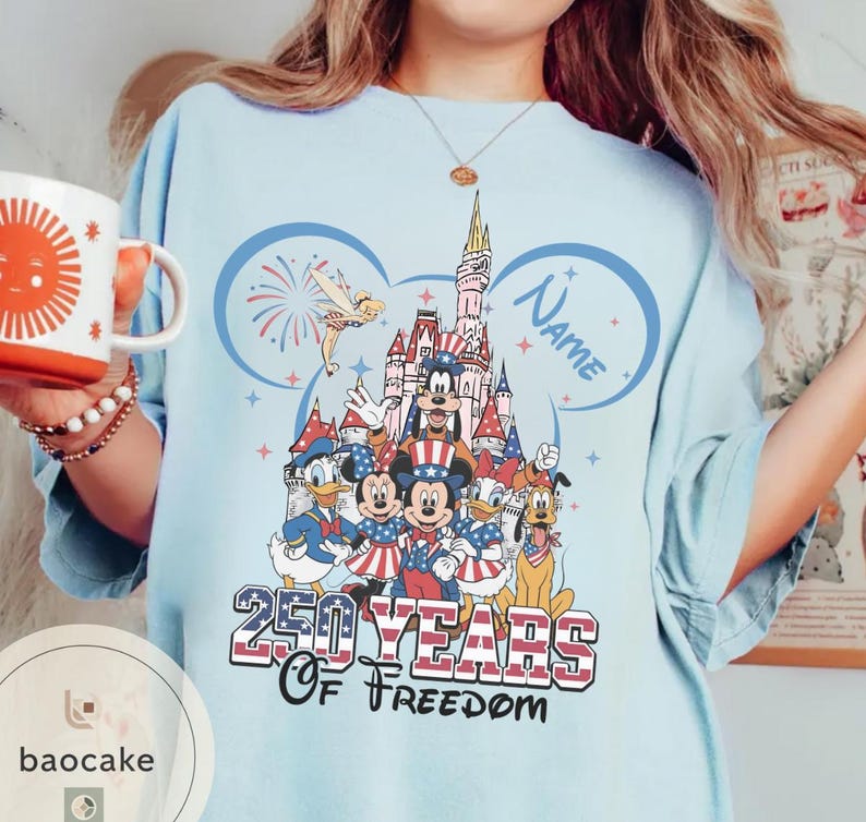 Peut inclure: T-shirt bleu clair avec un motif color&eacute; de personnages Disney devant un ch&acirc;teau, avec le texte "250 Years of Freedom". Le motif comprend Mickey Mouse, Donald Duck et d'autres personnages. Un nom peut &ecirc;tre ajout&eacute; au motif.