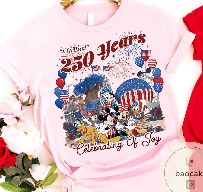 Puede incluir: Una camiseta rosa claro con un gr&aacute;fico colorido que celebra 250 a&ntilde;os. El dise&ntilde;o incluye Mickey Mouse, Minnie Mouse, Donald Duck y Pluto, junto con fuegos artificiales, globos y banderas americanas. El texto incluye "Oh Boy!" y "Celebrating Of Joy."
