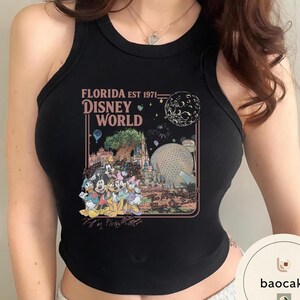 May include: A black sleeveless tank top featuring a graphic print with the text FLORIDA EST 1971 DISNEY WORLD and The Most Magical Place On Earth. The design includes illustrations of Disney characters, the castle, and the Epcot sphere.