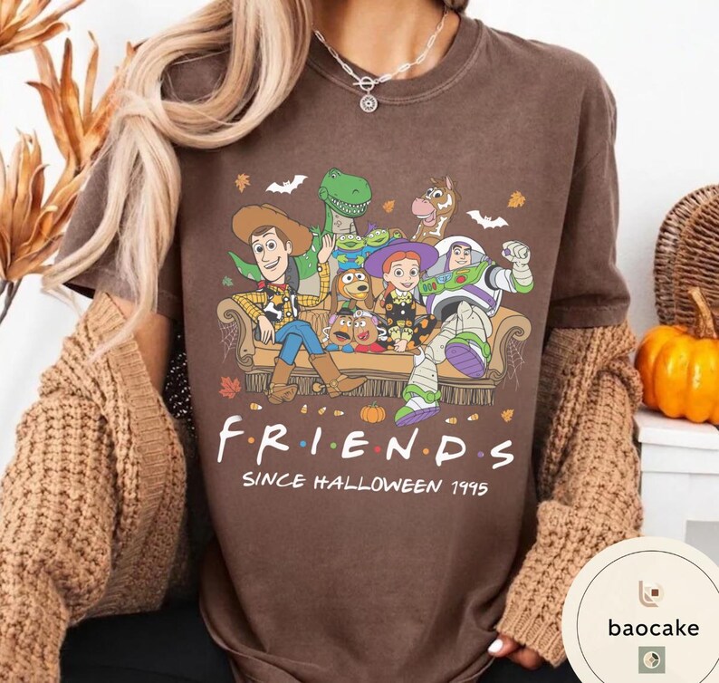 May include: A brown short-sleeve t-shirt featuring a graphic of Toy Story characters sitting on a couch with the text "FRIENDS SINCE HALLOWEEN 1995". The design includes Woody, Buzz Lightyear, Jessie, Rex, Slinky Dog, and Mr. Potato Head.