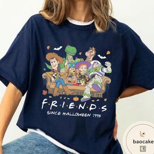 May include: A navy blue short-sleeve t-shirt featuring a graphic of Toy Story characters sitting on a sofa. The text reads F.R.I.E.N.D.S SINCE HALLOWEEN 1995. The design includes pumpkins, bats, and autumn leaves surrounding the characters on the couch.