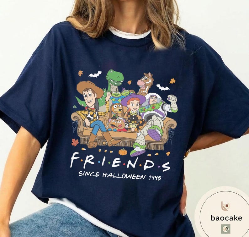 May include: A navy blue short-sleeve t-shirt featuring a graphic of Toy Story characters sitting on a sofa. The text reads F.R.I.E.N.D.S SINCE HALLOWEEN 1995. The design includes pumpkins, bats, and autumn leaves surrounding the characters on the couch.