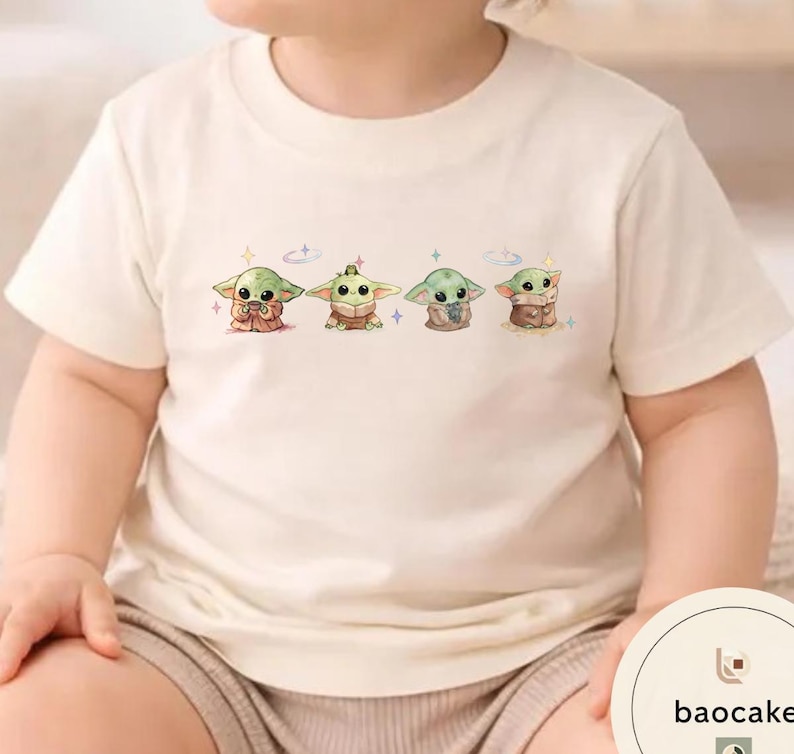 May include: Cream-colored t-shirt featuring a graphic of four cartoon characters. The characters are green with large eyes and are in different poses. The shirt is made of a soft material and is suitable for children.