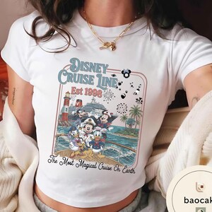 Puede incluir: Camiseta blanca con un gr&aacute;fico colorido de personajes de Disney en un crucero. El dise&ntilde;o incluye el texto "Disney Cruise Line Est 1998" y "The Most Magical Cruise On Earth."
