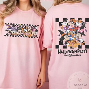 May include: Pink t-shirts featuring a Halloween-themed graphic. The front design showcases cartoon characters in Halloween costumes on a checkered background. The back of the shirt displays a larger group of characters with the text "Halloween Party" and "Walt Disney World".