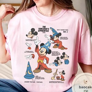 May include: Pink t-shirt featuring a graphic of Mickey Mouse as the Sorcerer's Apprentice, with text and illustrations from the 1940s. The design includes various poses and details, such as hand expressions and sleeve movement.