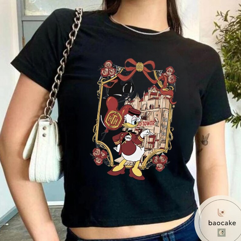 May include: Black t-shirt featuring a cartoon image of Donald Duck in a bellhop uniform, holding a balloon with the letters "HTH". The graphic includes a building, roses, and the words "Tower".