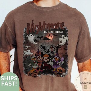 May include: Brown t-shirt with a Halloween-themed graphic. The graphic features cartoon characters dressed in costumes, ghosts, bats, and the text "Nightmare on Main Street".