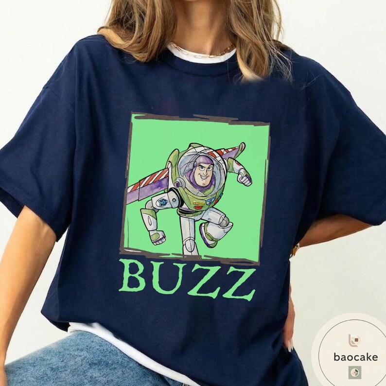 K&ouml;nnte beinhalten: Ein marineblaues T-Shirt mit einer quadratischen Grafik der Figur Buzz Lightyear in einem wei&szlig;en, gr&uuml;nen und violetten Raumanzug vor hellgr&uuml;nem Hintergrund. Das Wort BUZZ ist in gro&szlig;en, hellgr&uuml;nen Gro&szlig;buchstaben unter der Grafik aufgedruckt.