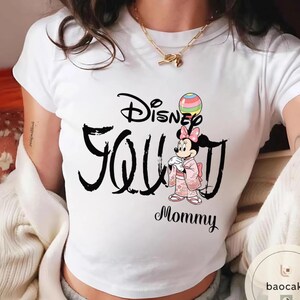 Puede incluir: Camiseta blanca con la frase "Disney Seoul Mommy" en escritura negra. La camiseta incluye una ilustraci&oacute;n de Minnie Mouse con un kimono rosa sosteniendo un globo colorido. Se ve un collar dorado.