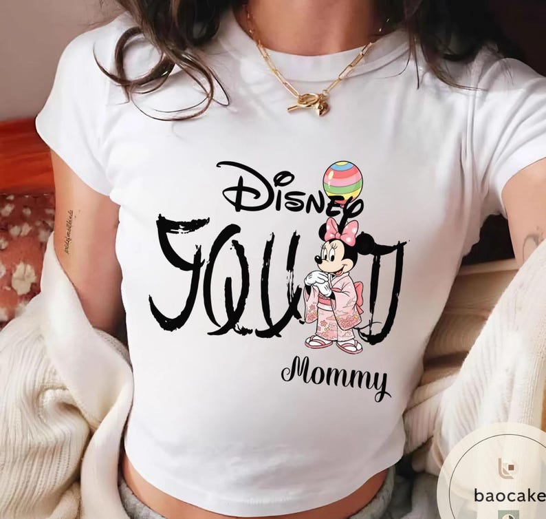 Puede incluir: Camiseta blanca con la frase "Disney Seoul Mommy" en escritura negra. La camiseta incluye una ilustraci&oacute;n de Minnie Mouse con un kimono rosa sosteniendo un globo colorido. Se ve un collar dorado.