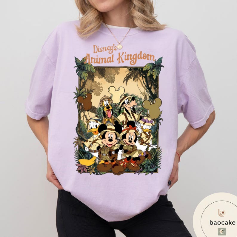 May include: A light purple t-shirt featuring a graphic of Disney's Animal Kingdom characters, including Mickey and Minnie Mouse, Donald Duck, and Goofy, in safari attire. The text "Disney's Animal Kingdom" is arched above the characters.