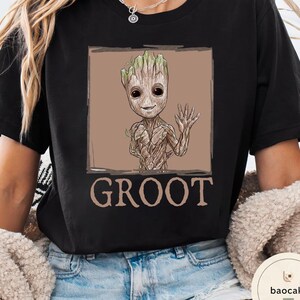 May include: Black t-shirt featuring a Groot graphic from Guardians of the Galaxy. The design shows Groot waving with a brown background and the word "GROOT" below. The shirt is a comfortable, casual style.