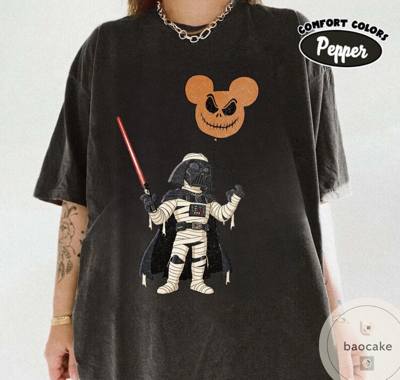 May include: Black t-shirt featuring a cartoon illustration of Darth Vader holding a lightsaber, with a Mickey Mouse-shaped Jack Skellington balloon. The shirt has the words "Comfort Colors Pepper" printed on it.
