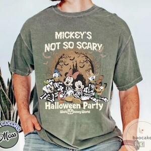 May include: Moss green t-shirt featuring a Halloween design with Mickey Mouse, Minnie Mouse, Donald Duck, Goofy, and Pluto dressed as skeletons. The shirt reads "Mickey's Not So Scary Halloween Party" with a spooky castle and bats.