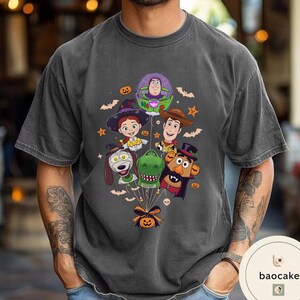 Pode incluir: Uma t-shirt cinzento-carv&atilde;o com uma impress&atilde;o gr&aacute;fica de personagens de Toy Story vestidos com fatos de Halloween, incluindo Buzz Lightyear, Jessie, Woody, Slinky Dog, Rex e Mr. Potato Head, todos ligados por fios a uma ab&oacute;bora.