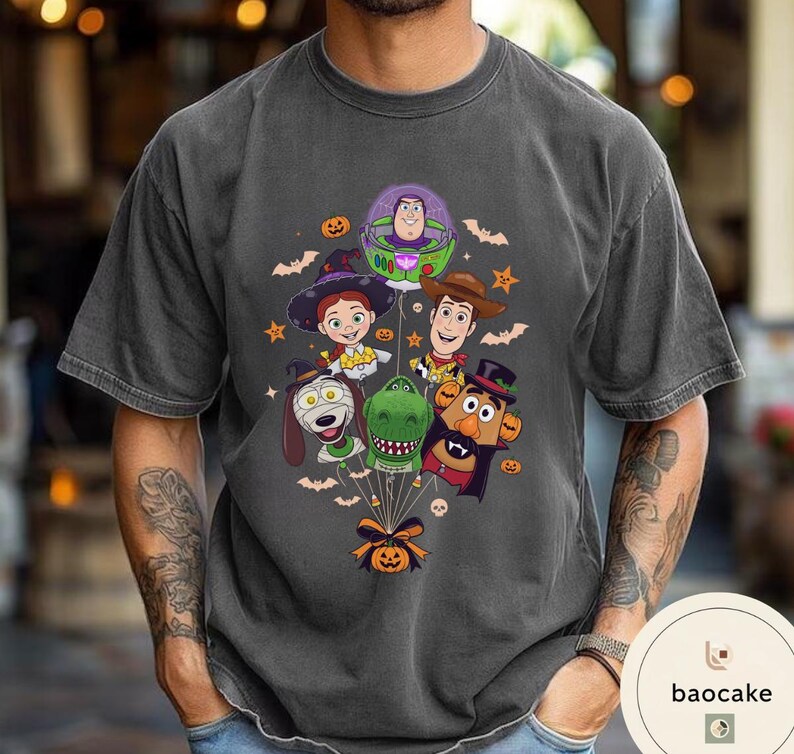 Pode incluir: Uma t-shirt cinzento-carv&atilde;o com uma impress&atilde;o gr&aacute;fica de personagens de Toy Story vestidos com fatos de Halloween, incluindo Buzz Lightyear, Jessie, Woody, Slinky Dog, Rex e Mr. Potato Head, todos ligados por fios a uma ab&oacute;bora.