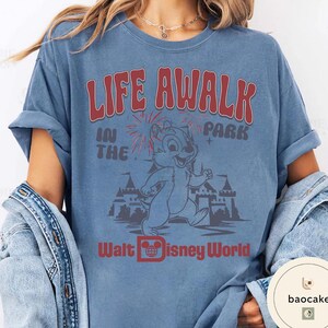 May include: Blue t-shirt with a graphic featuring Chip from Disney's Chip 'n Dale Rescue Rangers. The design includes the text "LIFE A WALK IN THE PARK" and "Walt Disney World" in red and white. The shirt has rolled-up sleeves.