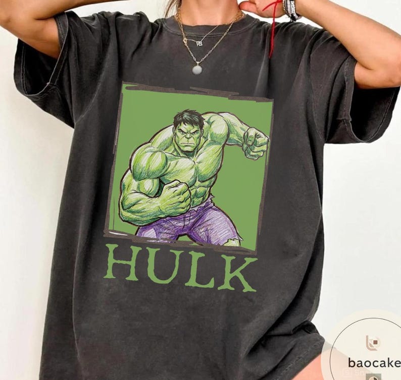 May include: Dark gray t-shirt featuring a green and purple illustration of the Hulk character. The illustration is set against a green background with the word "HULK" in green block letters below the image. The shirt has short sleeves.
