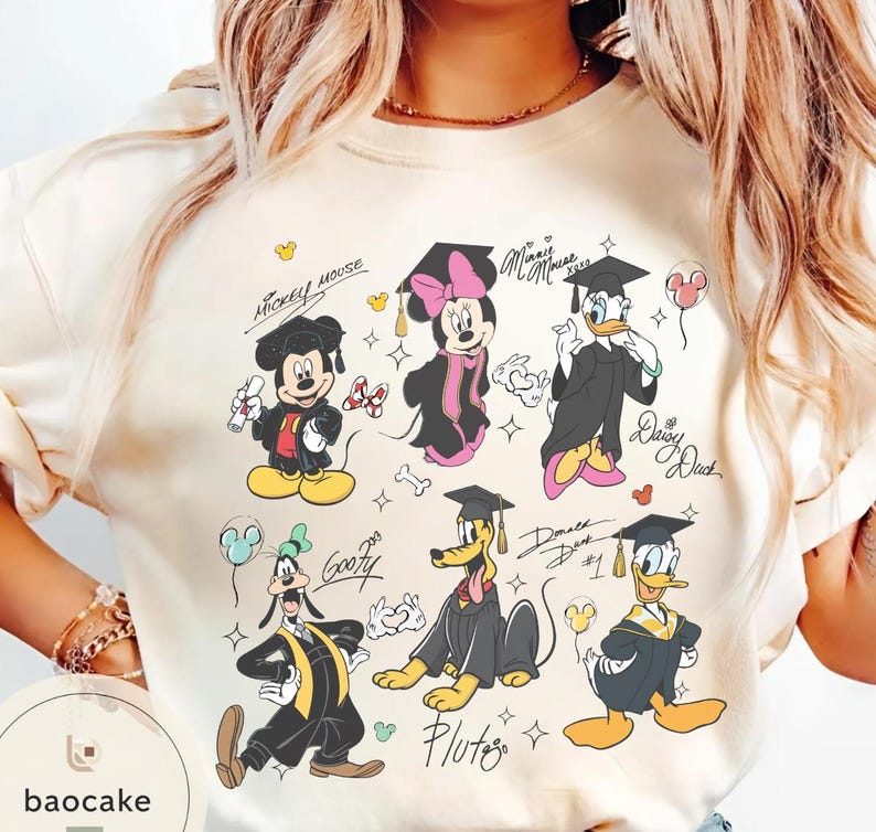 May include: Cream-colored t-shirt featuring cartoon characters Mickey Mouse, Minnie Mouse, Donald Duck, Daisy Duck, Goofy, and Pluto in graduation attire. Each character is wearing a graduation cap and gown. The shirt includes character names and signatures.