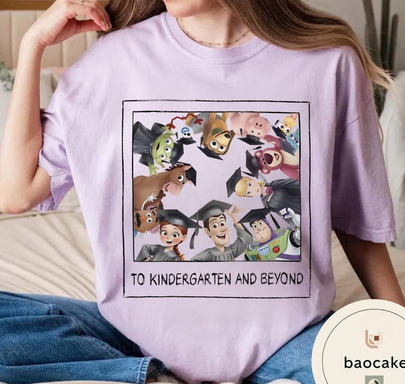 May include: A lilac t-shirt with a graphic of animated characters wearing graduation caps. The graphic is framed in a black rectangle and includes the text "TO KINDERGARTEN AND BEYOND".