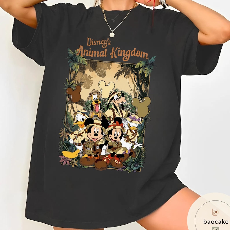 May include: Black t-shirt featuring a graphic of Disney's Animal Kingdom characters, including Mickey and Minnie Mouse, Donald Duck, and Goofy, in safari outfits. The text "Disney's Animal Kingdom" is displayed above the characters.