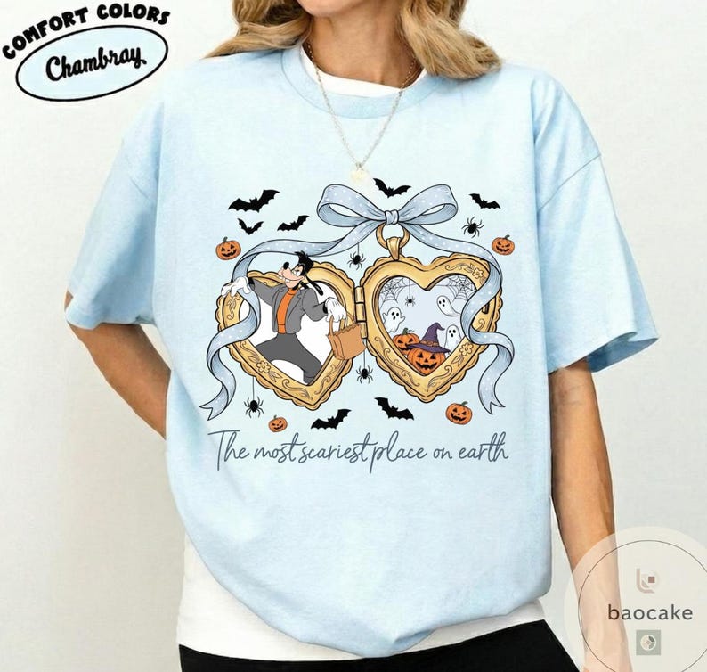 May include: Pale blue t-shirt with a Halloween graphic. The design includes two heart-shaped lockets with cartoon characters, bats, spiders, and pumpkins. The text on the shirt reads "The most scariest place on earth."