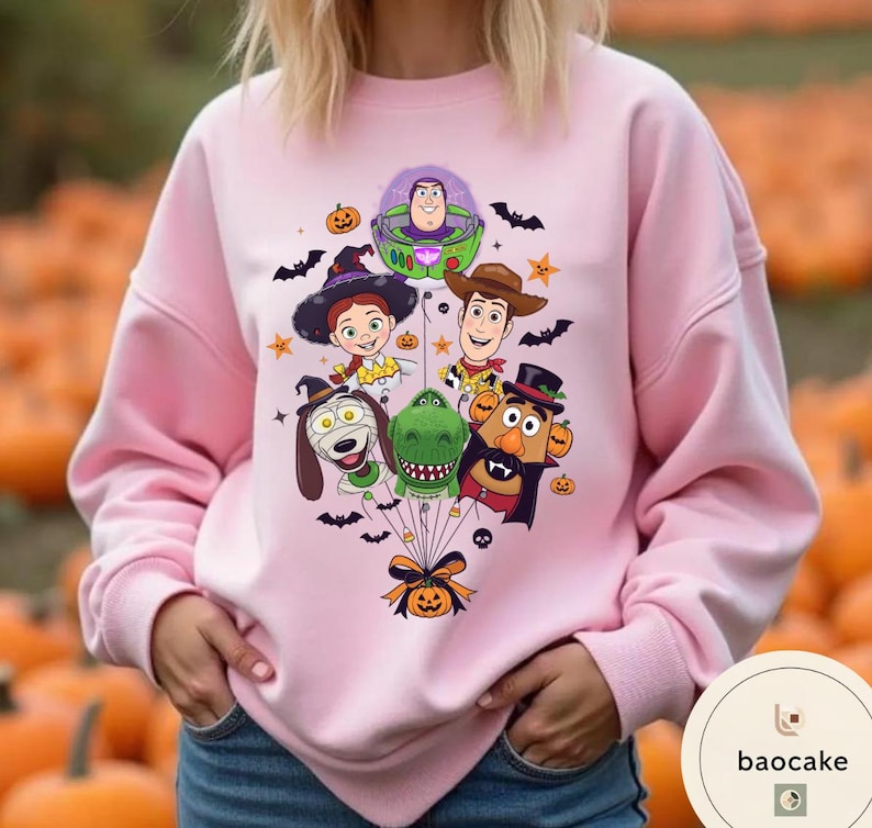 Pode incluir: Uma camisola rosa claro com uma impress&atilde;o gr&aacute;fica de personagens de Toy Story vestidos com fatos de Halloween, incluindo Buzz Lightyear, Woody, Jessie, Rex, Slinky Dog e Mr. Potato Head, todos atados a uma ab&oacute;bora com um la&ccedil;o preto.