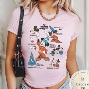 May include: A light pink t-shirt featuring a graphic of Mickey Mouse from "The Sorcerer's Apprentice" with various poses and text. The design includes a blue wizard hat, red robe, and text that reads "Walt Disney Prod RX-1".