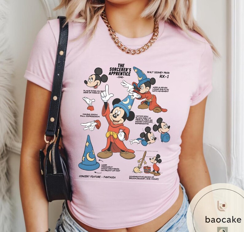 May include: A light pink t-shirt featuring a graphic of Mickey Mouse from "The Sorcerer's Apprentice" with various poses and text. The design includes a blue wizard hat, red robe, and text that reads "Walt Disney Prod RX-1".