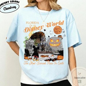 May include: Light blue t-shirt with a graphic featuring "Florida Disney World" and a Halloween theme. The design includes a castle, Mickey Mouse, pumpkins, and the text "The Most Scariest Place On Earth."