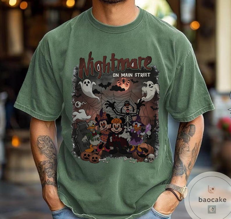 May include: Green t-shirt with a Halloween-themed graphic. The design features the text "Nightmare on Main Street" above cartoon characters, ghosts, bats, and pumpkins. The shirt is a solid green color.