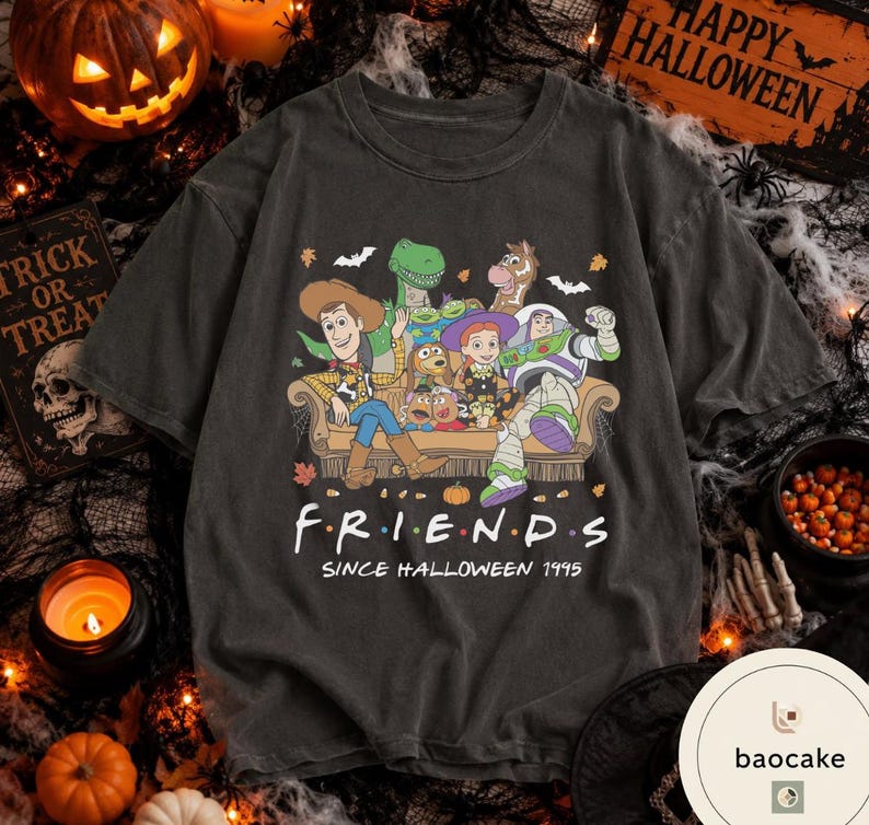 May include: A charcoal grey short-sleeve t-shirt featuring a graphic print of Toy Story characters sitting on a sofa. The text reads FRIENDS SINCE HALLOWEEN 1995. The design includes small pumpkins, bats, and autumn leaves surrounding the characters.