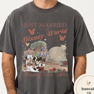 May include: Dark gray t-shirt featuring a Disney World design. The shirt has the words "Just Married Disney World" with Mickey and Minnie Mouse in wedding attire. The design includes a castle, Spaceship Earth, and roses.